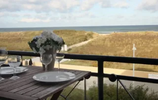 Runder Tisch mit zwei Stühlen und Blick auf die Ostsee, Balkon der Ferienwohnung mit Blumendeko und Gläsern.