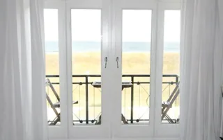 Blick durch Balkontür auf Strand, Wasser und Dünen in Warnemünde von der Villa am Strand aus.