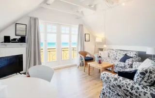 Heller Wohnbereich mit Sofa, Sessel, Tisch, rundem Esstisch und Fenster in der Ferienwohnung an der Ostsee
