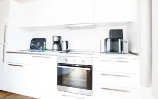 Voll ausgestattete moderne Küche mit Kaffeemaschine, Mikrowelle und Backofen in Weiß