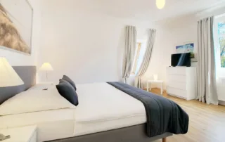 Helles Schlafzimmer mit Bett, Nachttischen, Lampen, Kommode und Fernseher in der Ferienwohnung